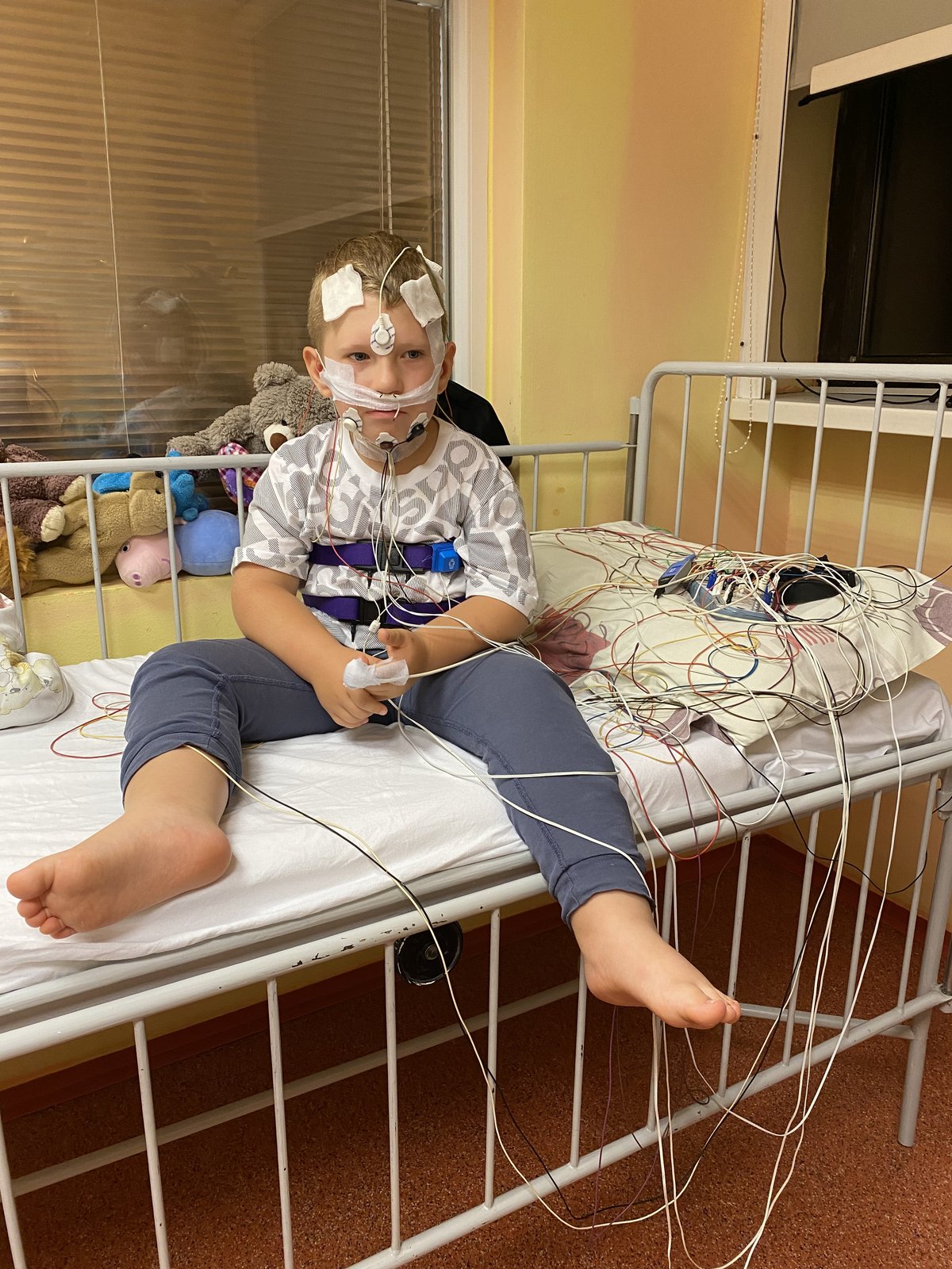 Leuško sedí na nemocničnej posteli počas EEG vyšetrenia so senzormi na hlave